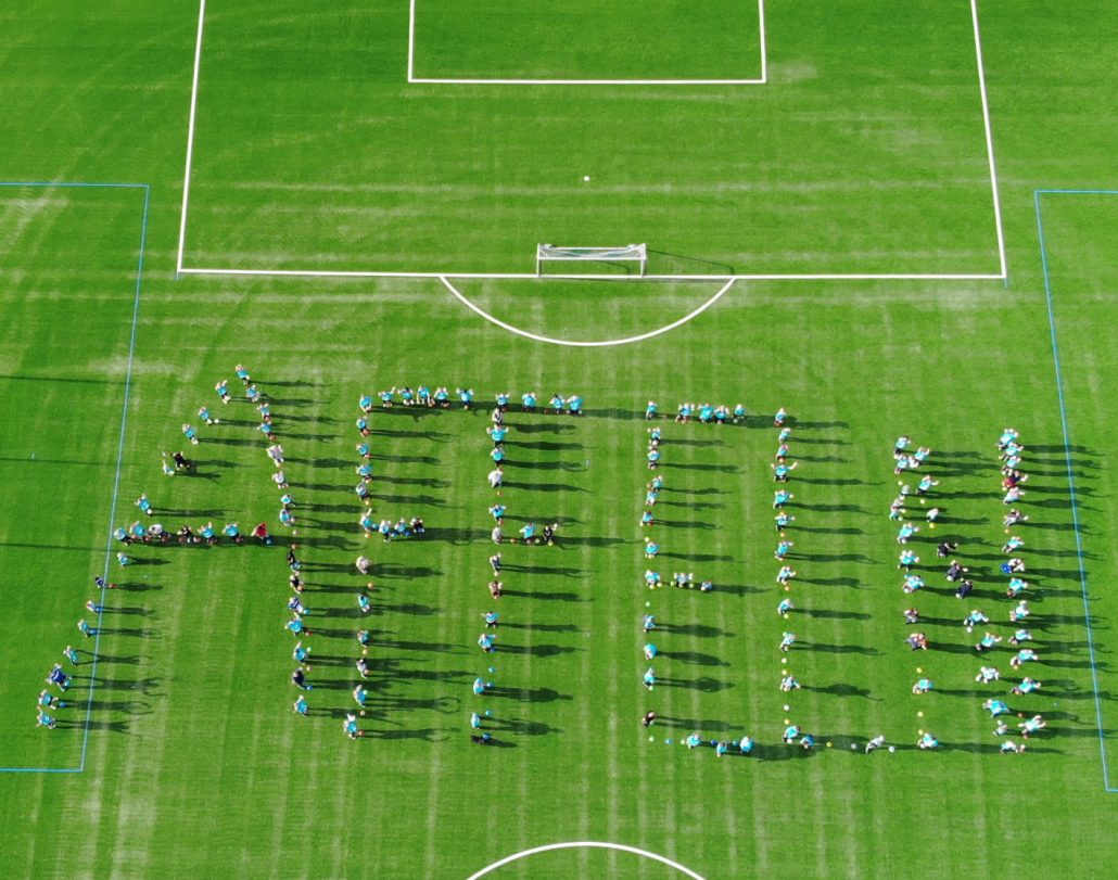 Viele Menschen, die auf einem Fußballfeld das Wort "Affeln" mit ihren Körpern gebildet haben