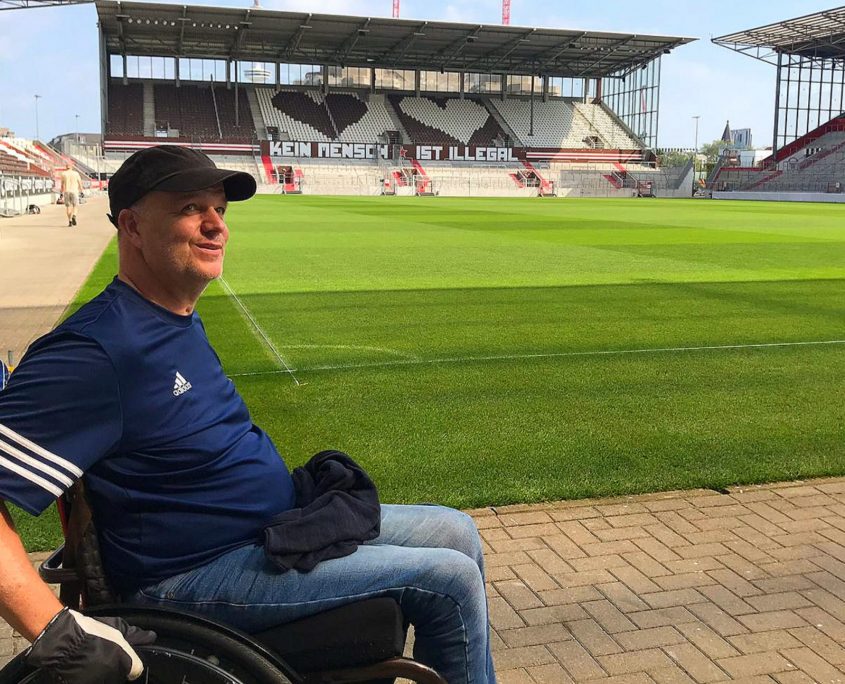 Ein Mann im Rollstuhl steht am Spielfeldrand des Millerntorstadions.