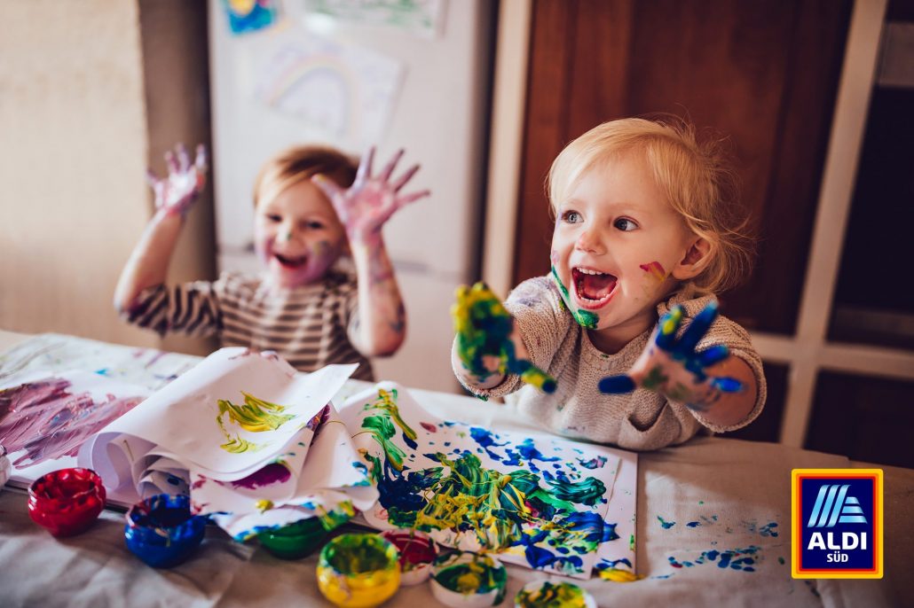 Foto von zwei Kleinkindern, die mit Fingerfarben bemalte Hände in die Höhe recken mit dem AldiSüd-Logo