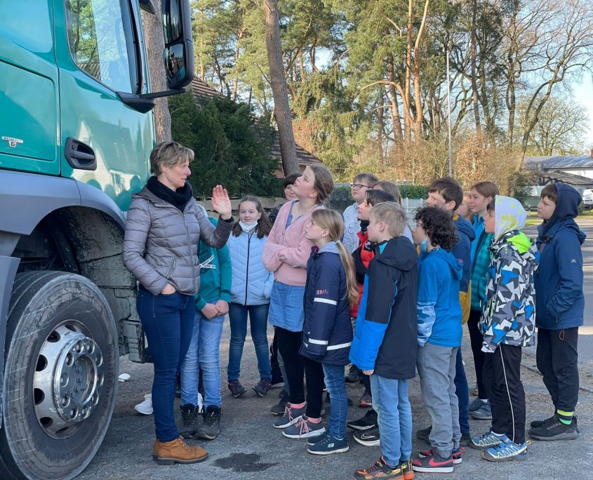 Eine Frau steht neben einem Lkw und erklärt einer Gruppe Kinder etwas.