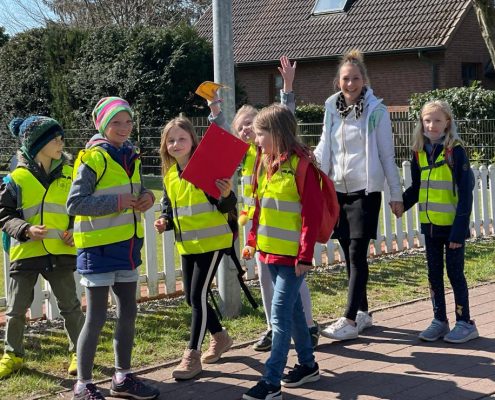 Eine junge Frau ist mit mehreren Kindern in Warnwesten zu Fuß unterwegs.