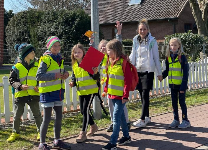 Eine junge Frau ist mit mehreren Kindern in Warnwesten zu Fuß unterwegs.