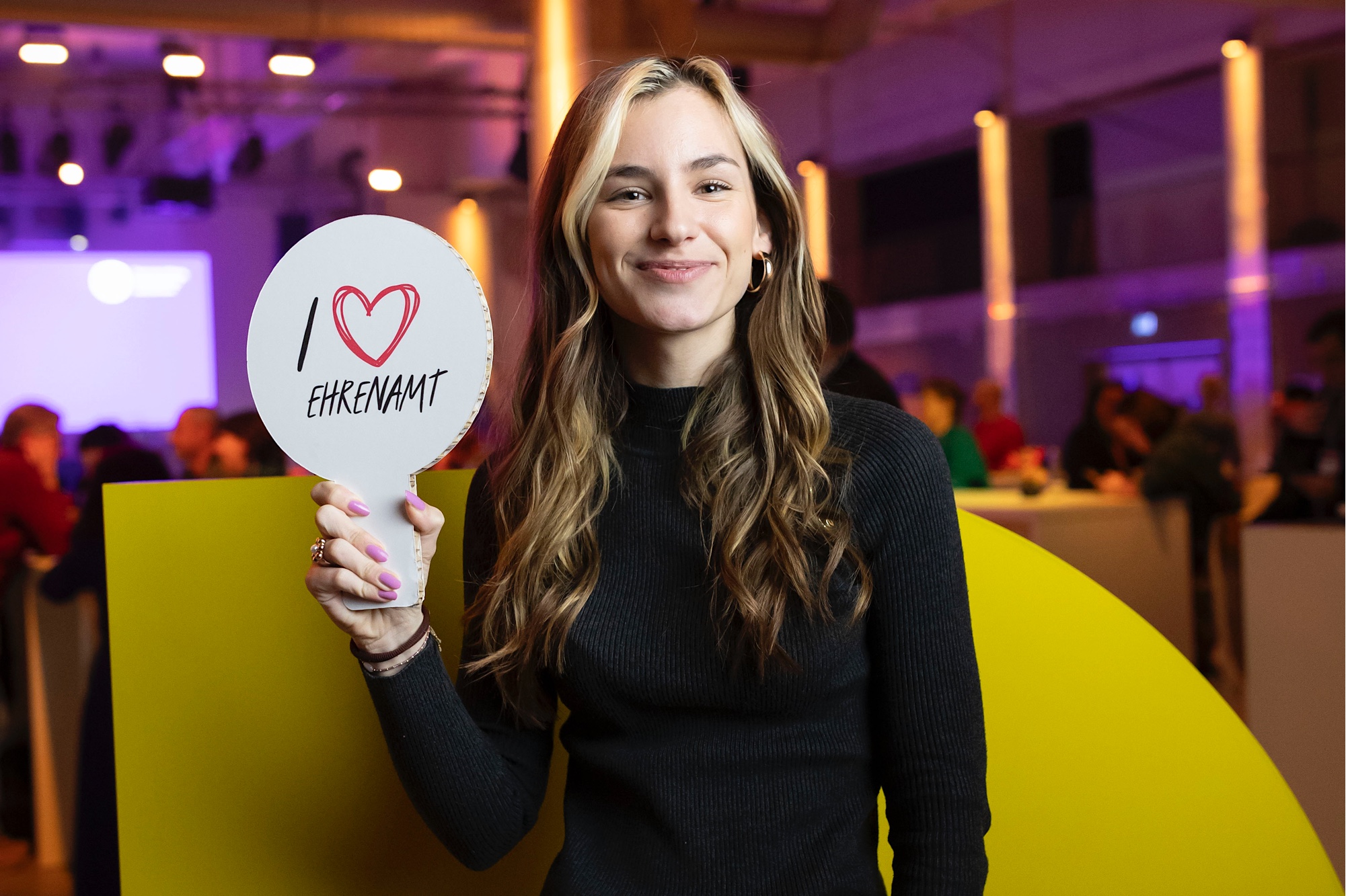 Eine Frau hält ein Schild in der Hand. Auf dem steht "Ich liebe Ehrenamt"