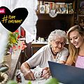 Foto von einer älteren und einer jungen Frau, die nebeneinander sitzen und gemeinsam auf einen Computer schauen. Ein gezeichnetes Herz mit dem Text: Danke #TeamEhrenamt