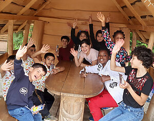 Kinder des ELa-Netzwerks "Förderverein Ehra-Lessien, ein Dorf - ein Team e.V." sitzen in einer Picknickhütte und winken in die Kamera.