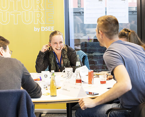 Junge Engagierte sitzen bei einem FuturE-Workshop an einem Tisch und tauschen sich gut gelaunt aus.