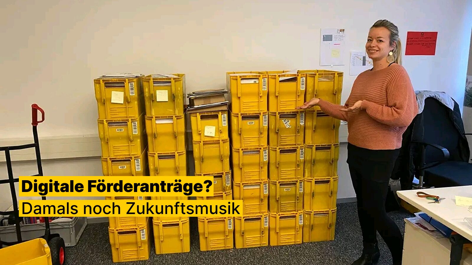 Eine Kollegin zeigt einen Stapel von Postkörben mit Förderanträgen