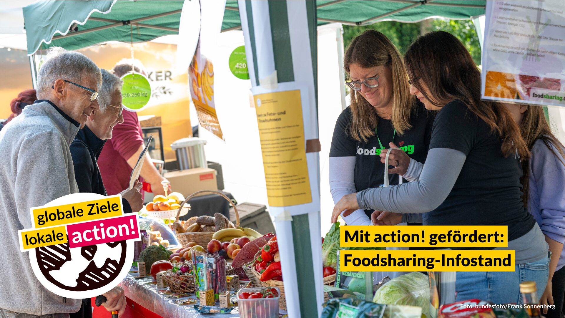 251024_action_Projektbeispiel Foodsharing_2 Menschen stehen an einem Foodsharing-Infostand auf einem Markt. Auf dem Tisch liegen viele gerettete Lebensmittel wie Obst, Gemüse und Brot. Infomaterialien und Banner sind sichtbar. Im Vordergrund sind die Logos „globale Ziele, lokale action!“ und „Mit action! gefördert: Foodsharing-Infostand“ zu sehen.