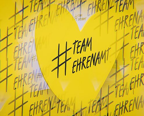 Symbolgrafik mit einem Herz und der vielfachen Beschriftung "# Team Ehrenamt" (zusammengeschrieben)