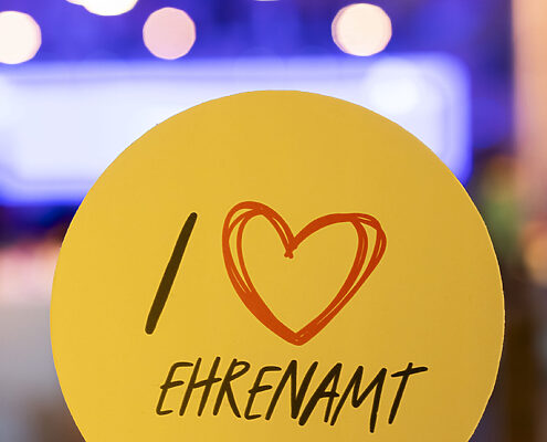 Hochgehaltenes Pappschild mit der Beschriftung "I Herzsymbol Ehrenamt"