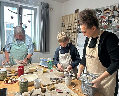 Drei Personen arbeiten zusammen an einem Tisch im Töpferkurs und formen gemeinsam Tonobjekte.