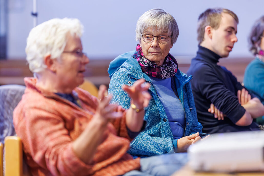 Personen sitzen in einer Gesprächsrunde, eine Person spricht und gestikuliert mit den Händen.